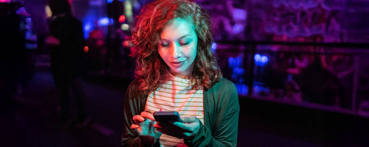 Junge Frau schaut auf ihr Smartphone und nutzt unbegrenztes Datenvolumen.