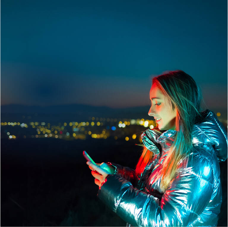 Frau schaut lächelnd vor einer nächtlichen Kulisse und nutzt ihre unlimited SIM-Karte